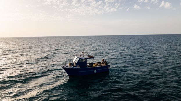 A solitary fishing boat floats on a calm ocean under a serene sky during early morning light.