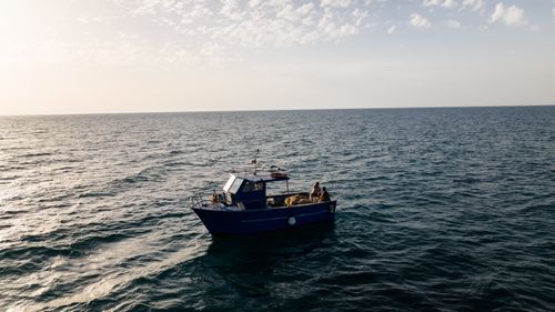 Free A solitary fishing boat floats on a calm ocean under a serene sky during early morning light. Stock Photo