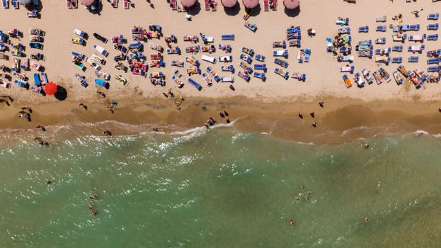 A high-angle aerial shot of a lively beach with colorful sun loungers and people enjoying the sun.