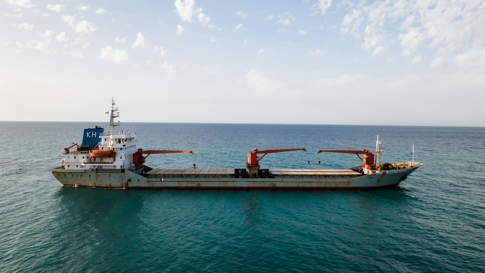 Aerial view of a cargo ship sailing in calm blue ocean under a clear sky.
