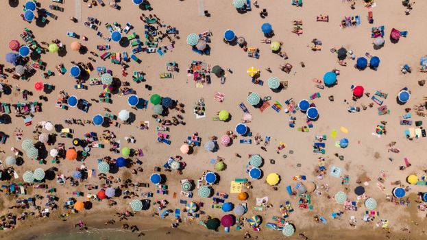 Vibrant aerial view of a crowded beach with colorful umbrellas and sunbathers.