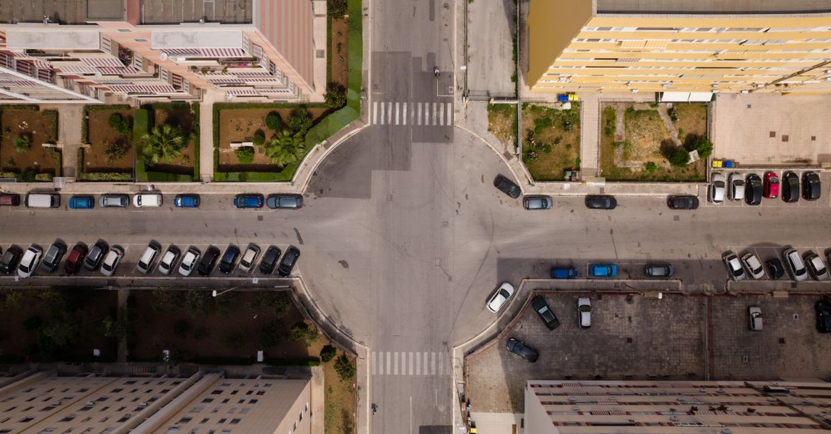Aerial view of city intersection with parked cars and residential buildings.