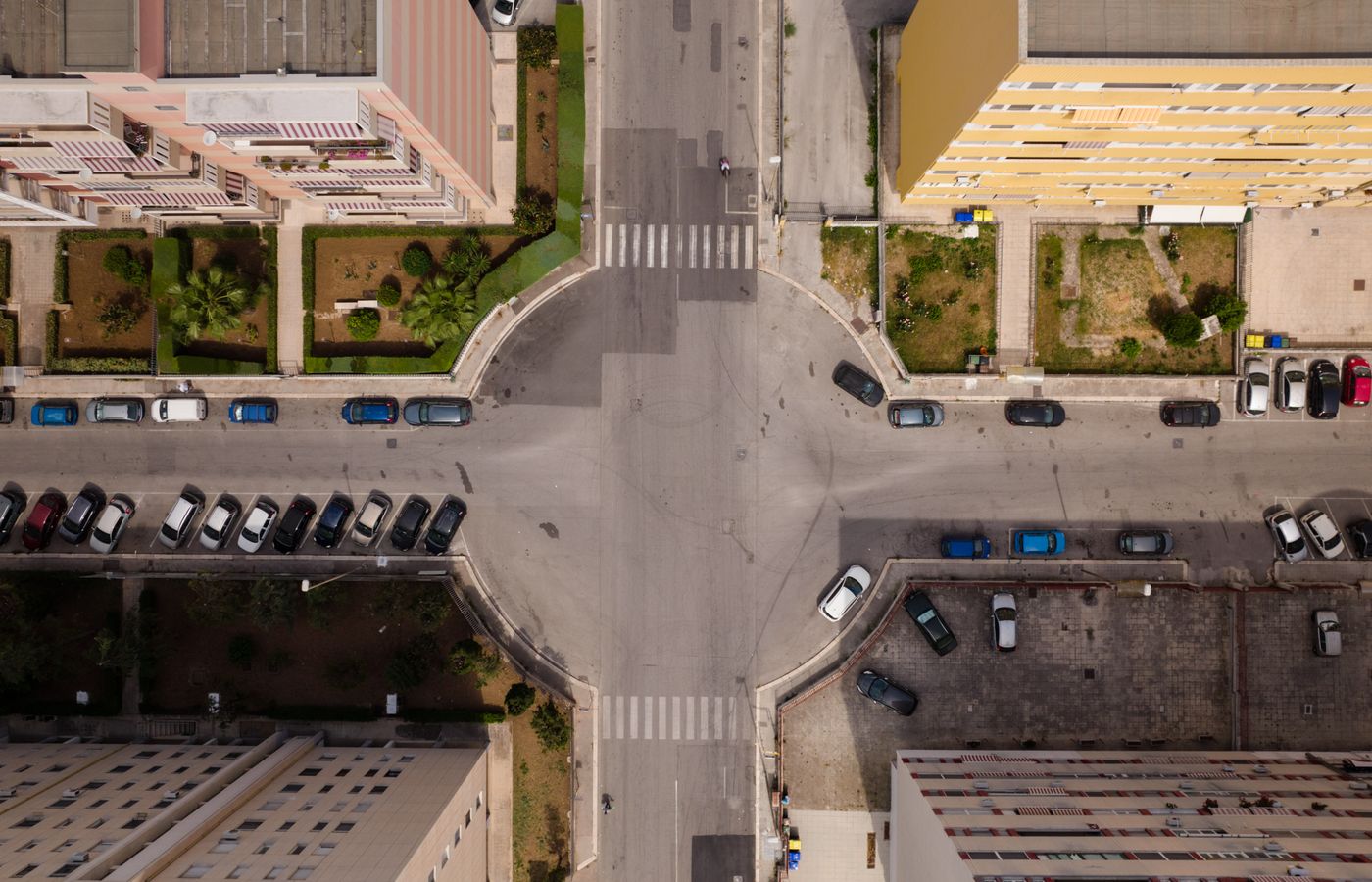 Aerial view of city intersection with parked cars and residential buildings.