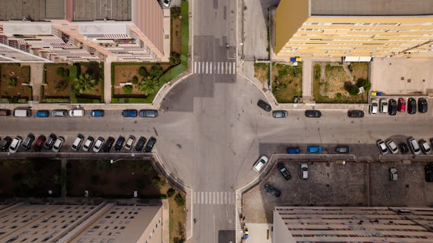 Aerial view of city intersection with parked cars and residential buildings.