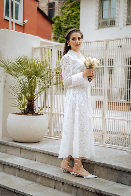 Free Elegant young woman posing in a white dress with a bouquet, standing on stairs outdoors. Stock Photo