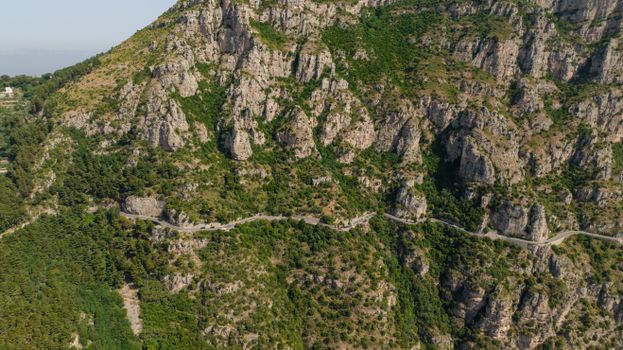 Stunning aerial shot of a winding road navigating a rugged mountain cliffside blanketed in greenery.