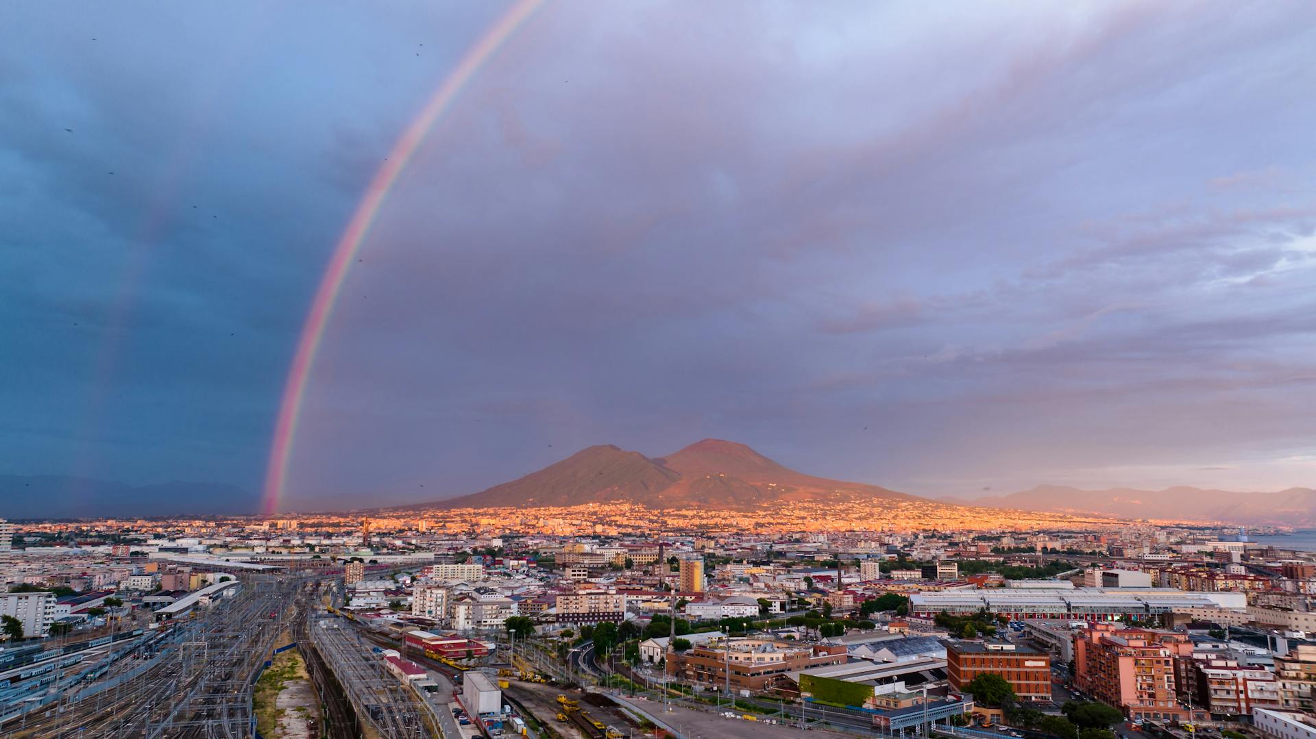 A breathtaking view of a rainbow over Naples cityscape with Mount Vesuvius in the backdrop.