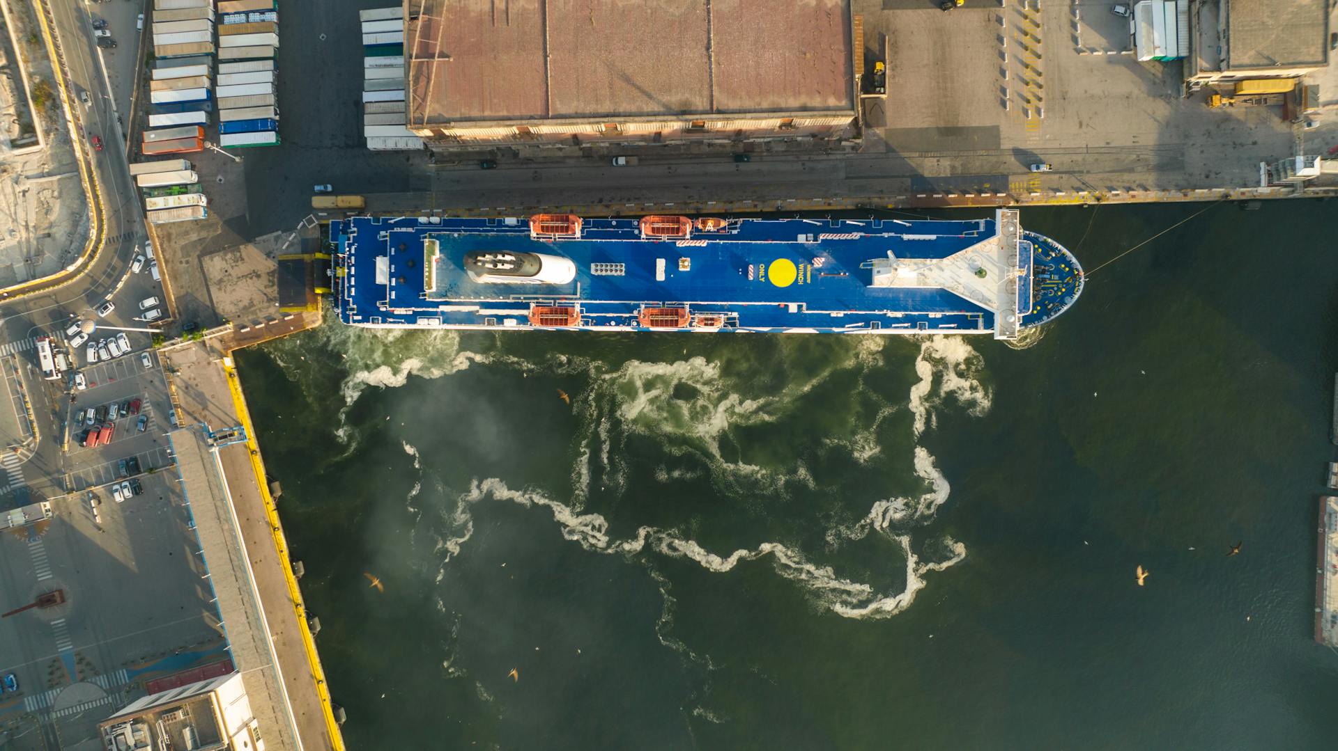 Aerial view of a cargo ship docked at an industrial port with visible harbor infrastructure.