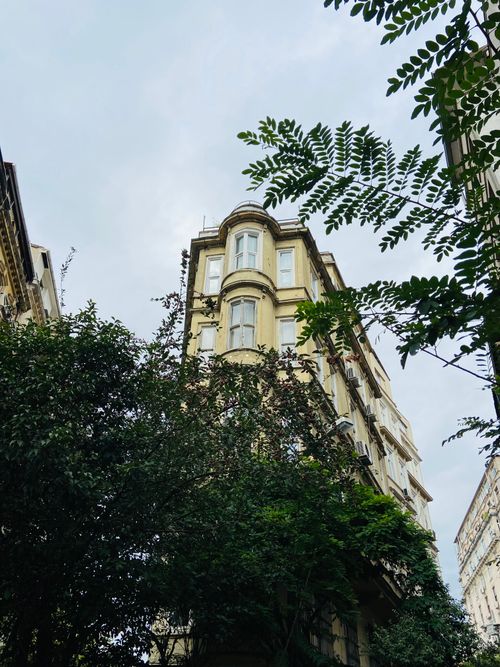 Free Low-angle shot of a historic building surrounded by lush greenery with a cloudy sky backdrop. Stock Photo