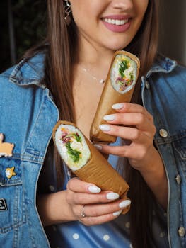 Close-up of a woman in a denim jacket holding artistic sushi wraps with vibrant ingredients.