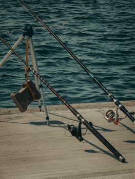 Fishing rods arranged on a concrete pier by the water, evoking leisure and hobbyist vibes.