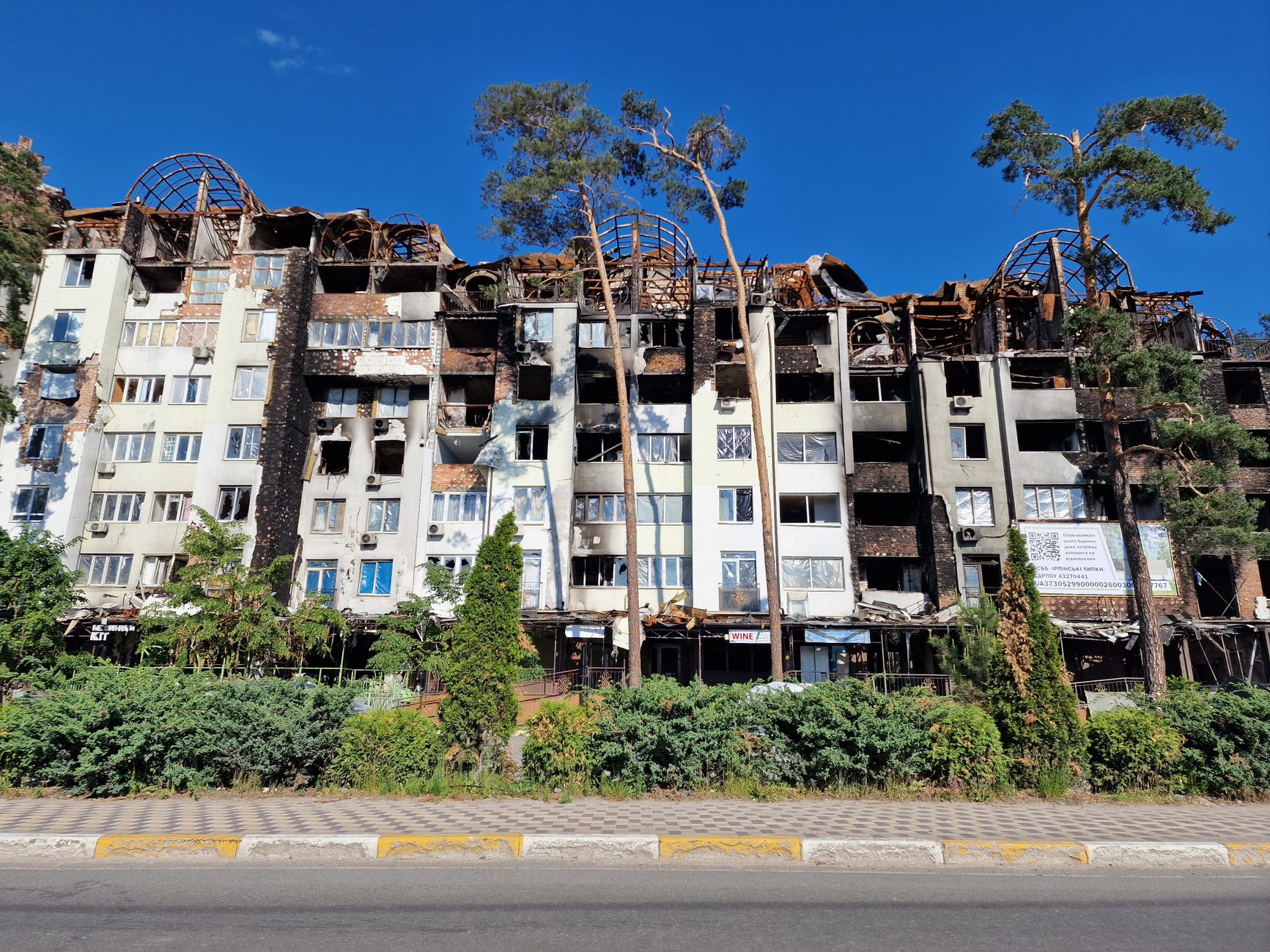 Exterior view of a ruined apartment building in Irpin, Ukraine under a clear blue sky.