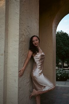 Stylish woman in a silk dress poses gracefully under an archway, radiating elegance and glamour.