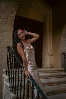 Woman poses gracefully in a satin dress by a stone staircase, exuding elegance.