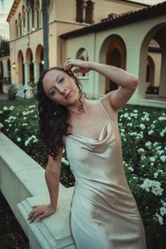 A woman in a flowing silk dress poses elegantly near a historical building with arches.