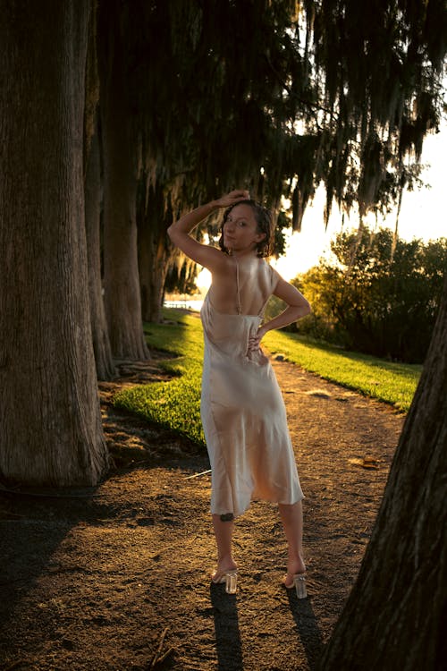 A Woman in Spaghetti Strap Dress and High Heels Near Tree Trunks