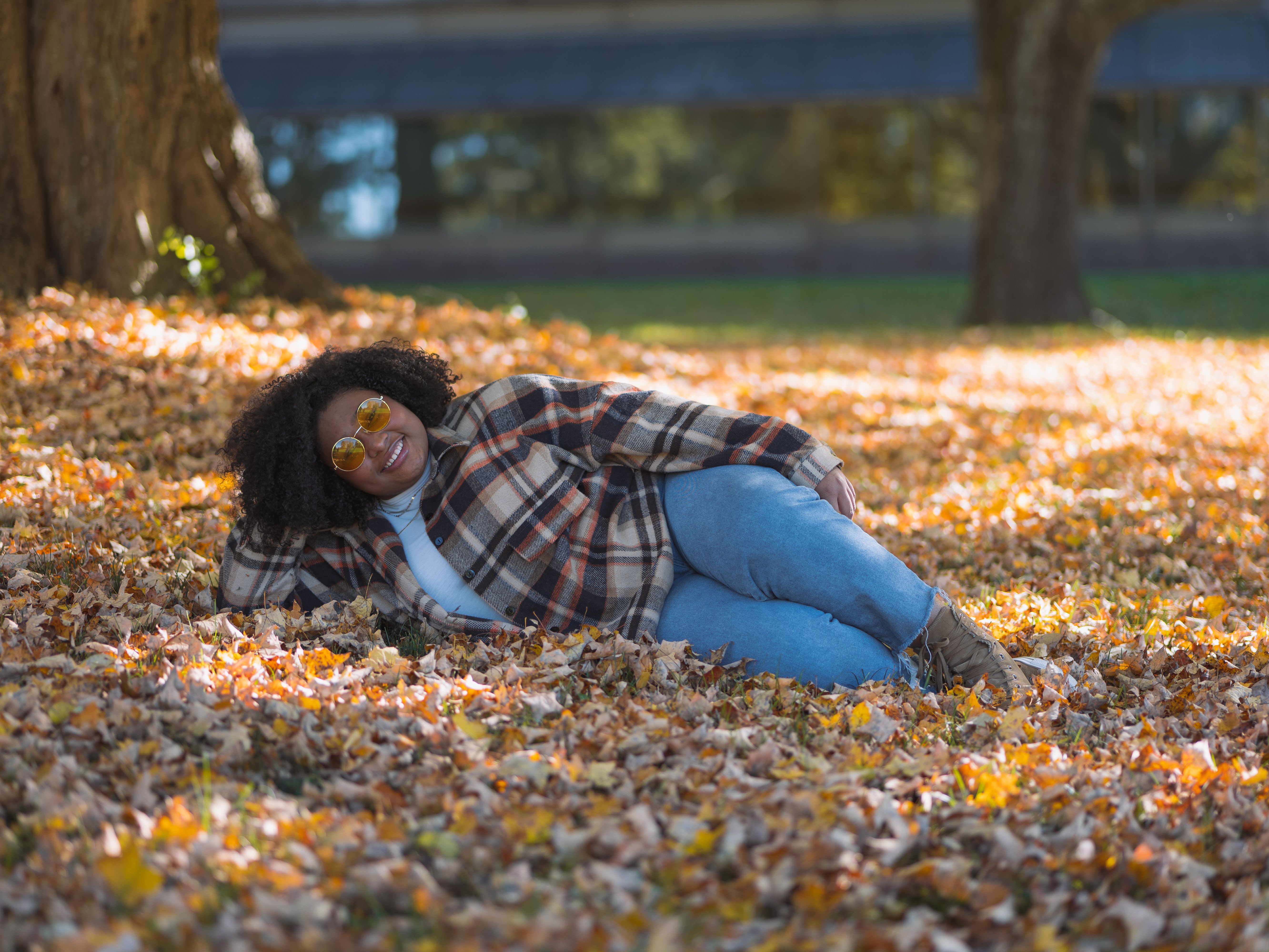 Woman in a plaid flannel shirt and jeans resting on fallen autumn leaves