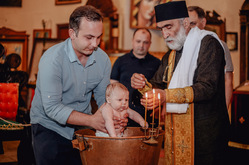 Free Baptism ceremony with a priest lighting candles, surrounded by family, indoors. Stock Photo