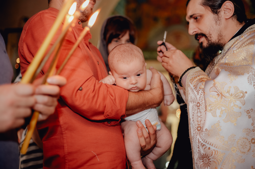 Free A baby is cradled during a traditional baptism ceremony involving candles and a priest. Stock Photo