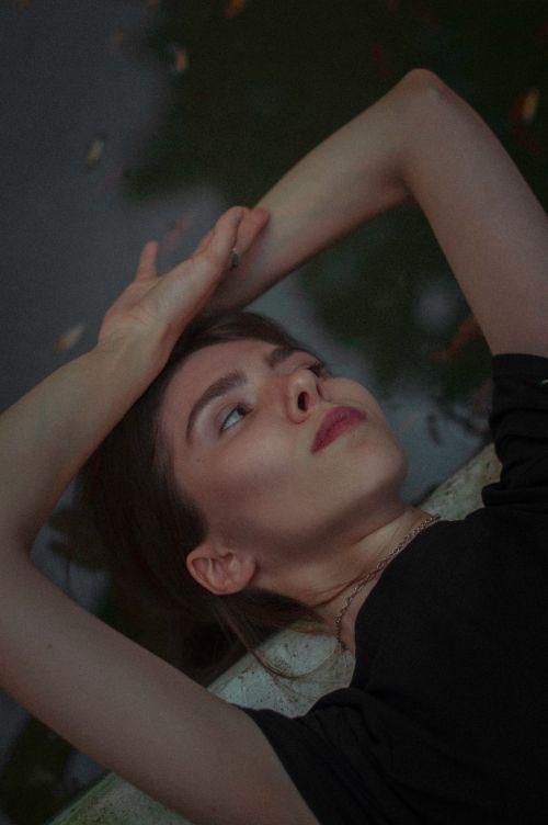 Free Young woman lying by a pond, arms raised, reflecting outdoors in serene nature setting. Stock Photo