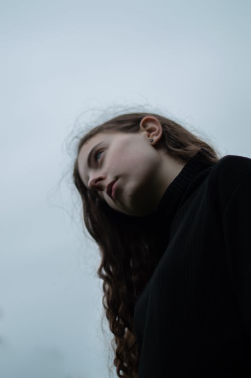Free Low-angle portrait of a young woman with curly hair against a cloudy sky. Stock Photo