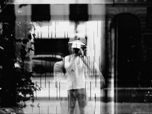 Free Black and white reflection of a man in a cap taking a picture through a window. Stock Photo