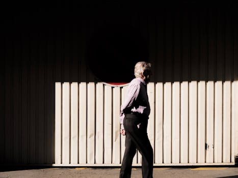 A senior man walks by a sunlit wall, casting a long shadow.