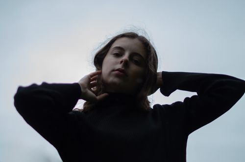 Free Low angle portrait of a young woman with hands on hair against a moody sky. Stock Photo