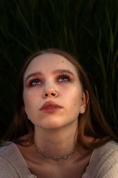 Free A woman with a nose piercing gazes upwards in a nature setting. Perfect for lifestyle themes. Stock Photo