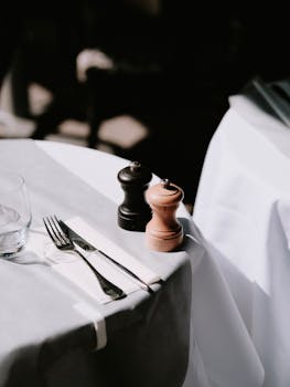 Minimalistic table setting featuring cutlery and pepper mills on a sunlit table.