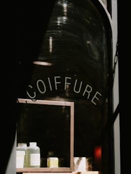 Moody shot of a coiffure shop's window reflecting hair products, emphasizing vintage storefront vibes.