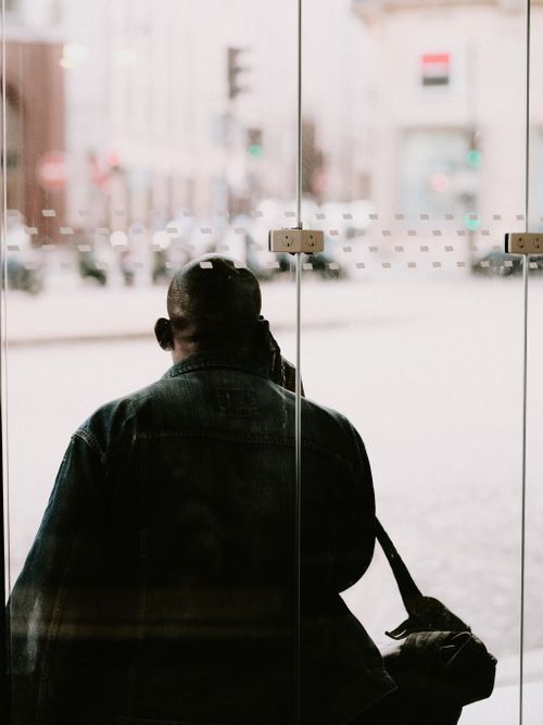 Free Back view of a man looking through a glass doorway onto a bustling street. Stock Photo