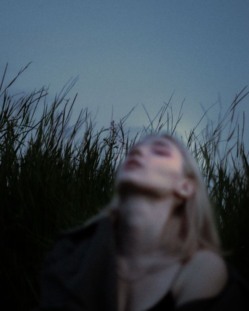Free Blurred silhouette of a woman with sky and grass backdrop at dusk. Stock Photo