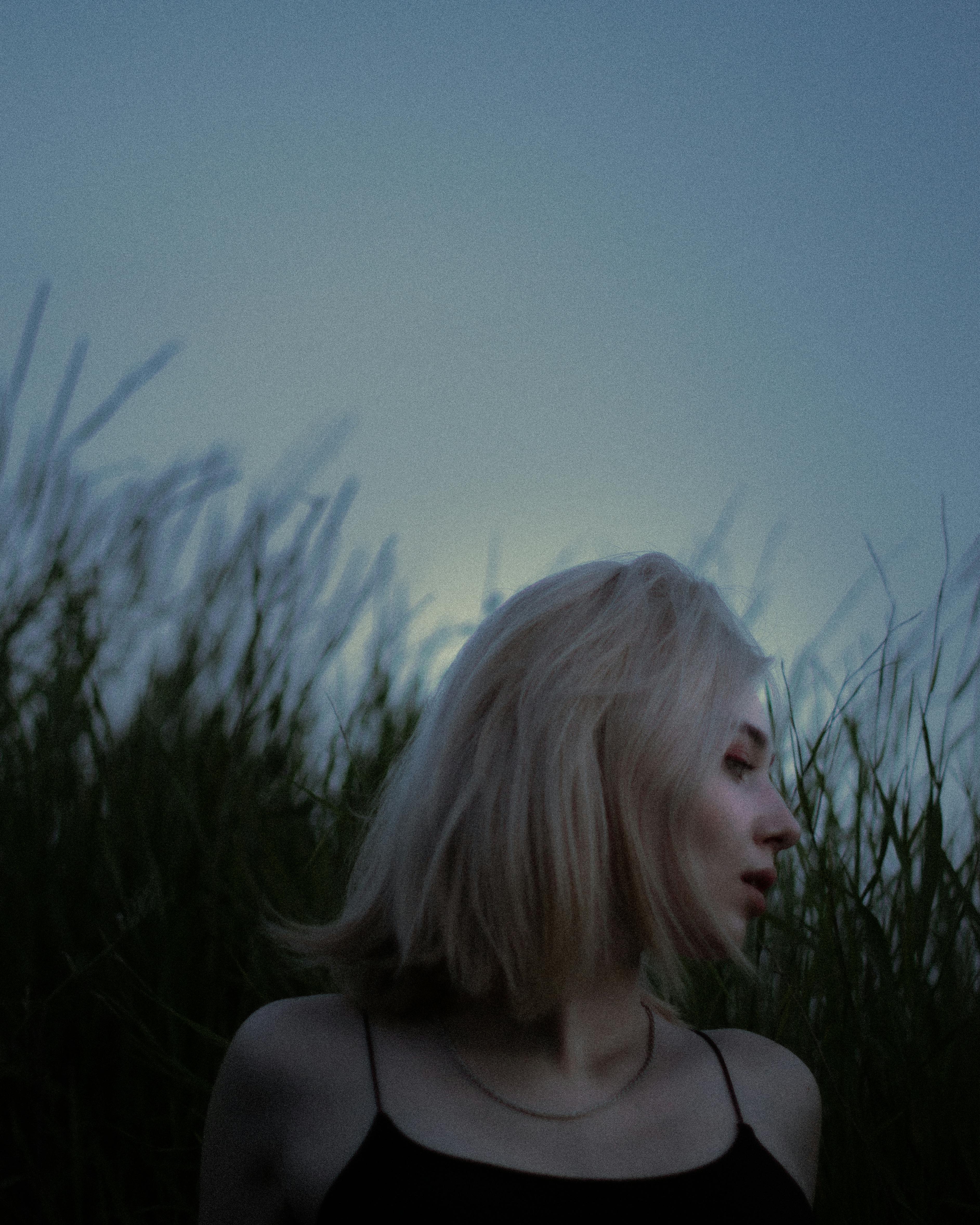 Mysterious silhouette of a woman standing amidst tall grass during twilight. Captivating and serene.