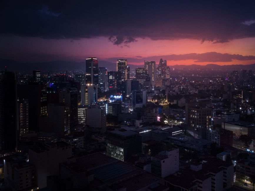 Aerial view of Mexico City's skyline at dusk with a vibrant sunset, showcasing skyscrapers and city lights.