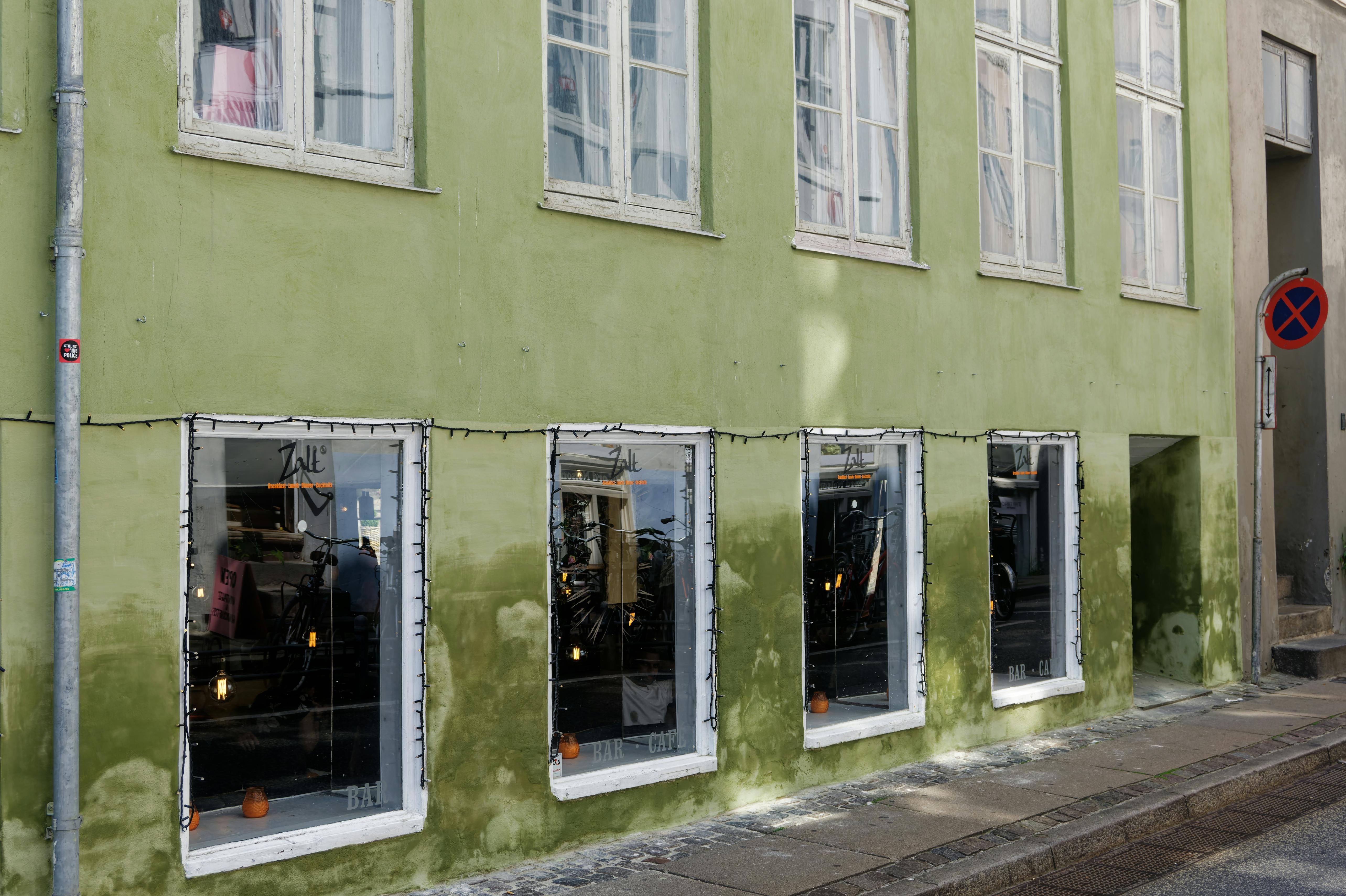 Green building facade in Copenhagen with large windows and urban street elements, captured in daylight.