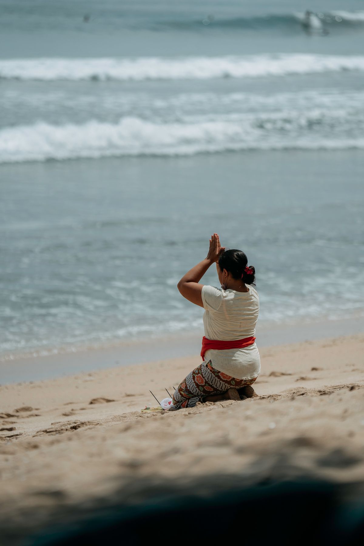 Bali - femeie în ținută tradițională se roagă pe plaja Kuta