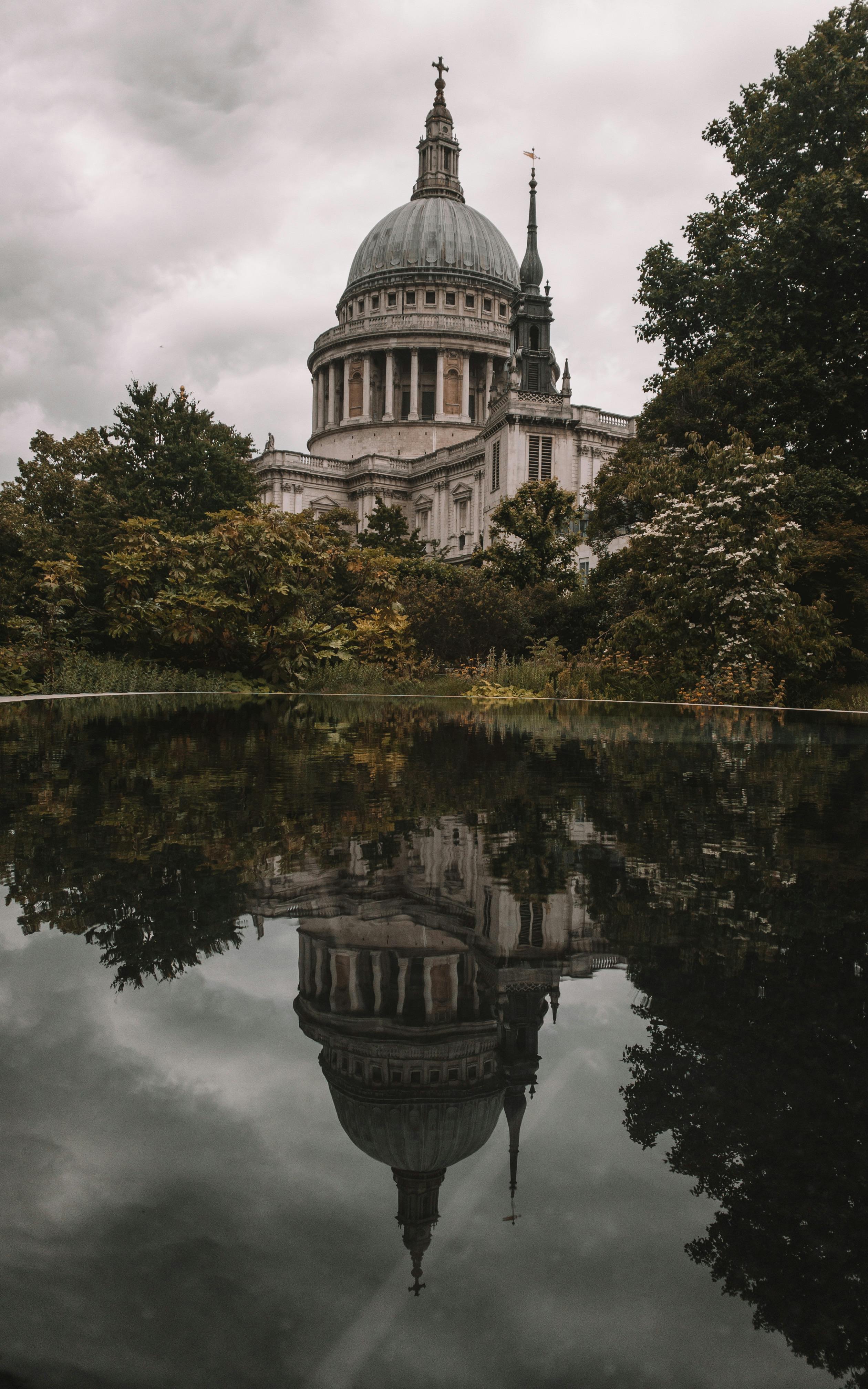 Stunning view of St. Paul's Cathedral reflecting in serene water amidst lush greenery in London.