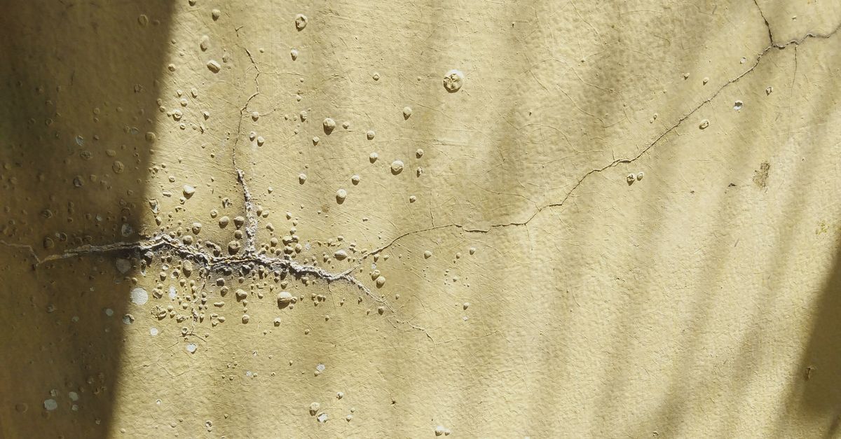Nahaufnahme einer rissigen, strukturierten Wand mit Schatten und sichtbaren Abnutzungsspuren