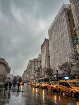 Street view of New York City with yellow taxis on a rainy day, highlighting urban life.