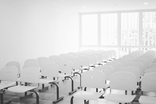 Free A bright, vacant conference room featuring rows of white chairs and natural light streaming through large windows. Stock Photo