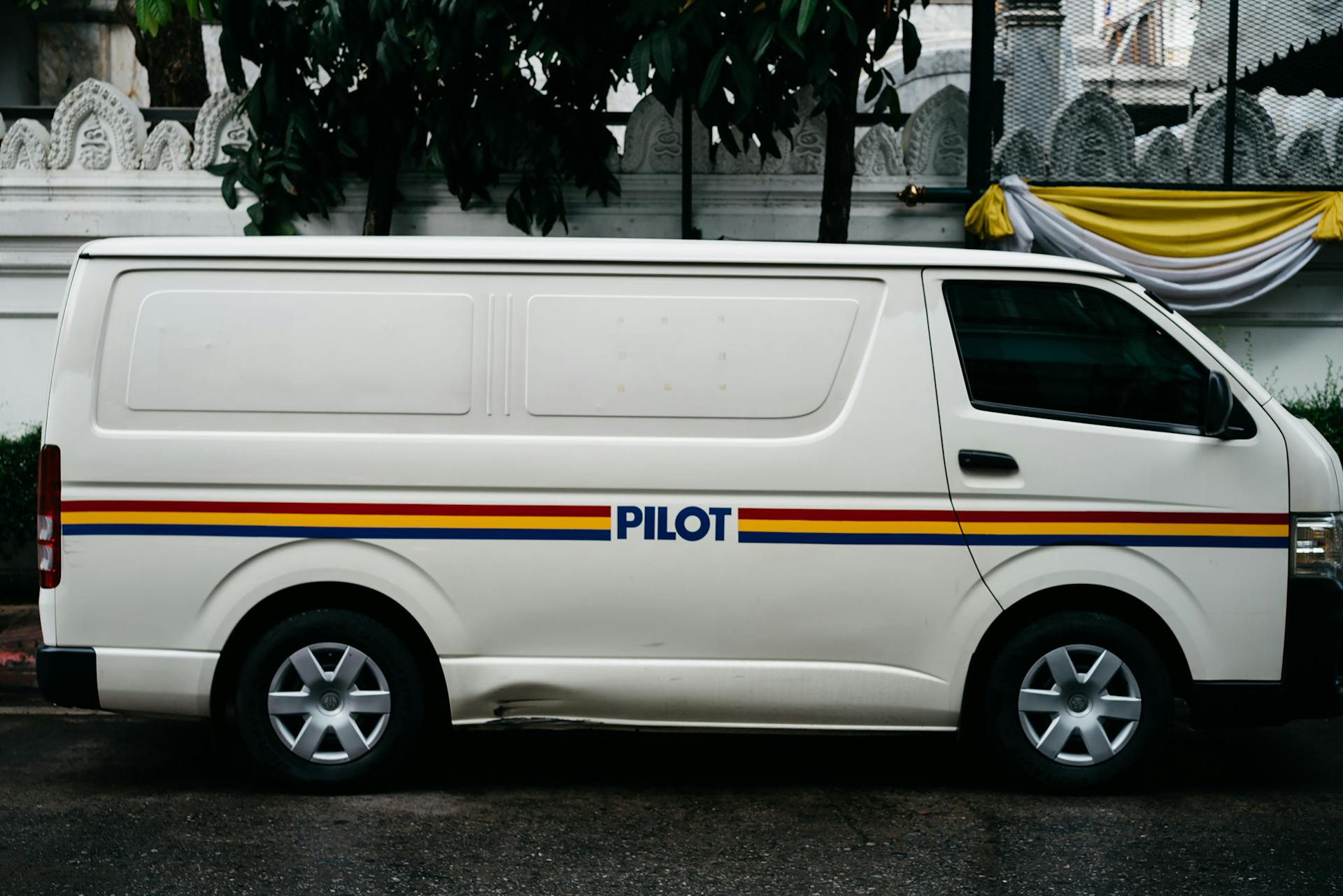 A parked white van with 'PILOT' branding, seen in an urban environment.