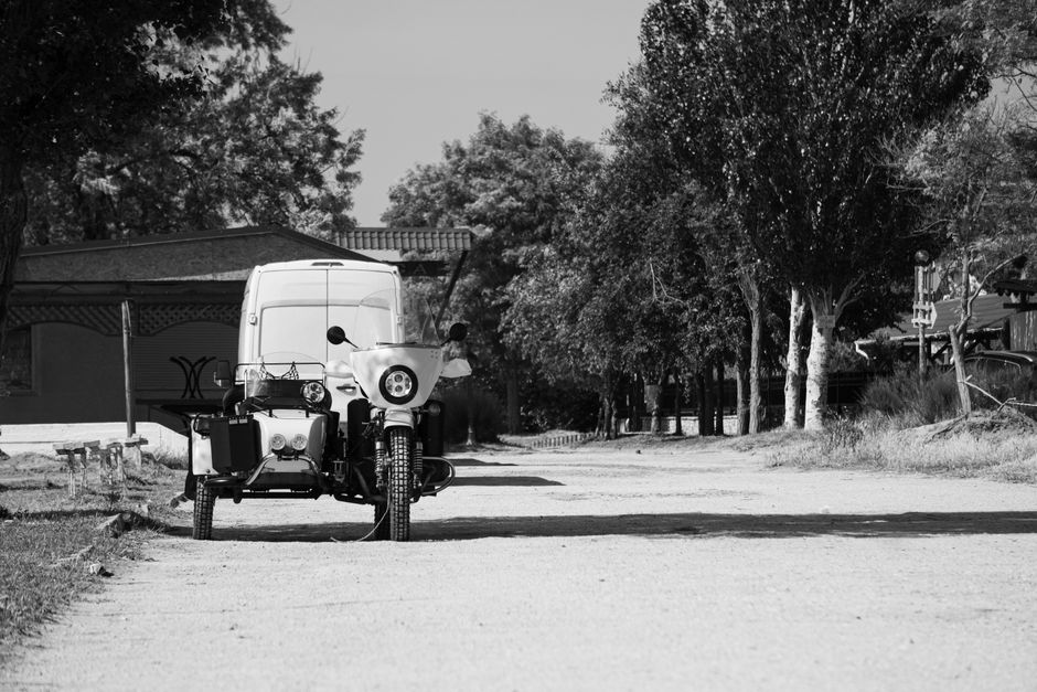 Black and white photo of a vintage motorcycle with sidecar parked on a quiet rural street.