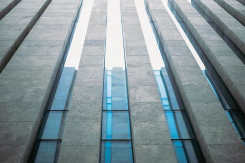 Free A striking low angle view of a modern building facade showcasing vertical glass panels between stone structures. Stock Photo