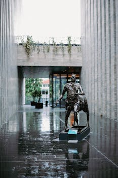 Striking bronze sculpture in a sleek architectural space on a rainy day.