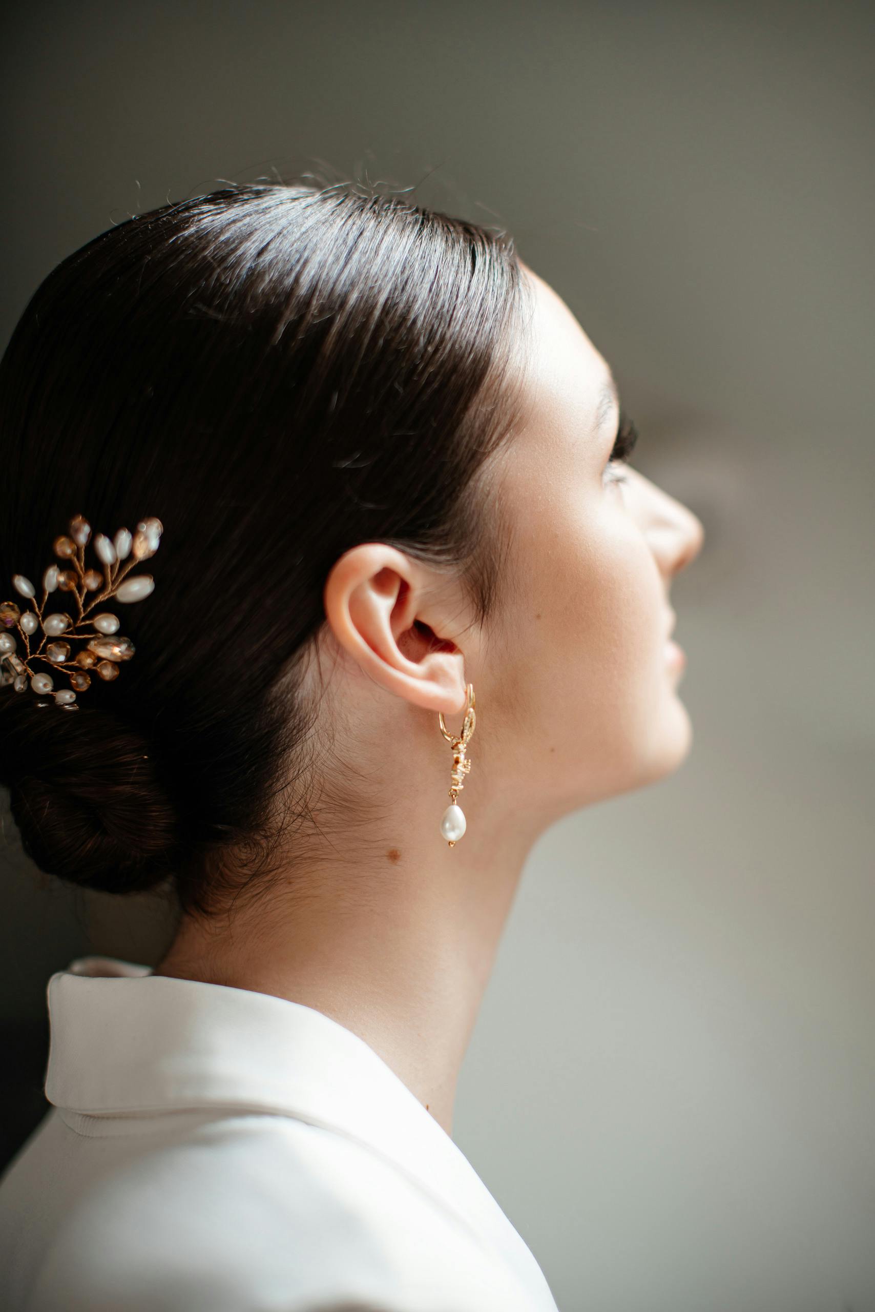 Side profile of a woman with ornate gold hairpin and pearl earring, elegantly styled hair.