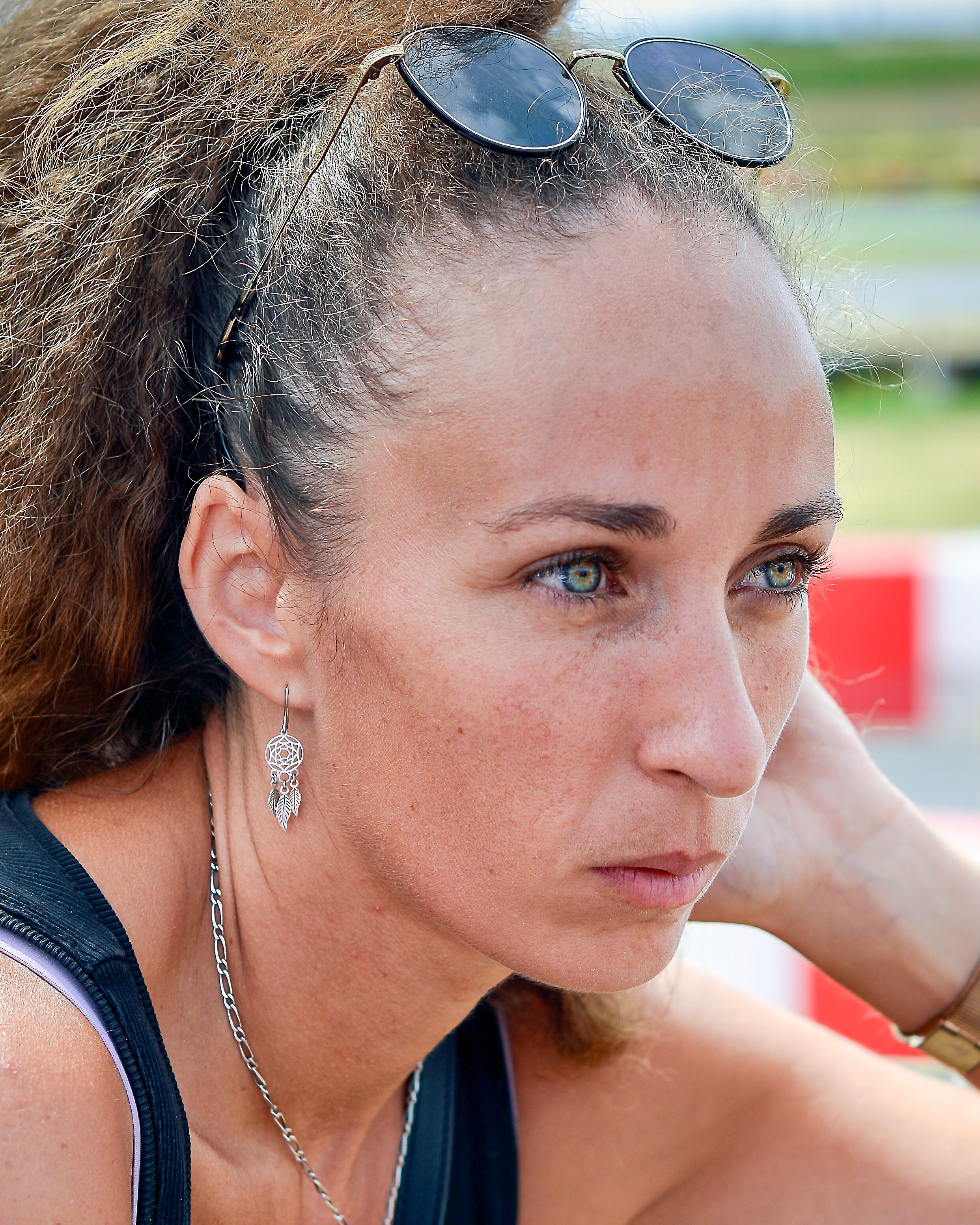Close-up portrait of a woman wearing sunglasses and jewelry outdoors.