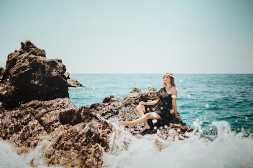 Woman Sitting on Rock at Sea