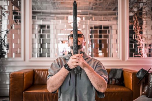 Man wearing sunglasses holding a vintage sword indoors with ornate decor in the background.