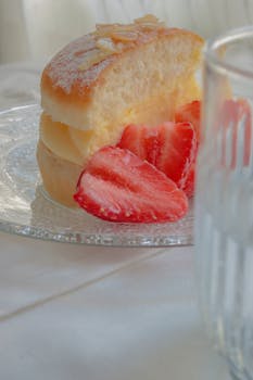 Scrumptious slice of cream cake with fresh strawberries on a glass plate, perfect dessert setting.